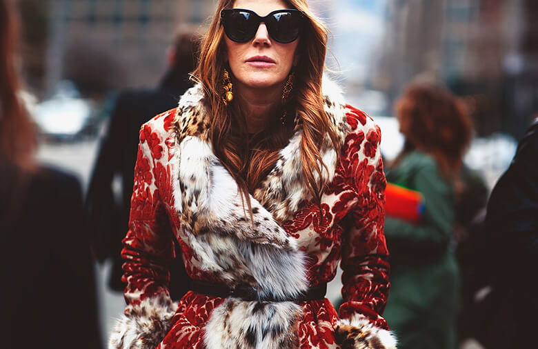 Anna Dello Russo posando para foto com casaco de pelo vermelho e óculos de sol
