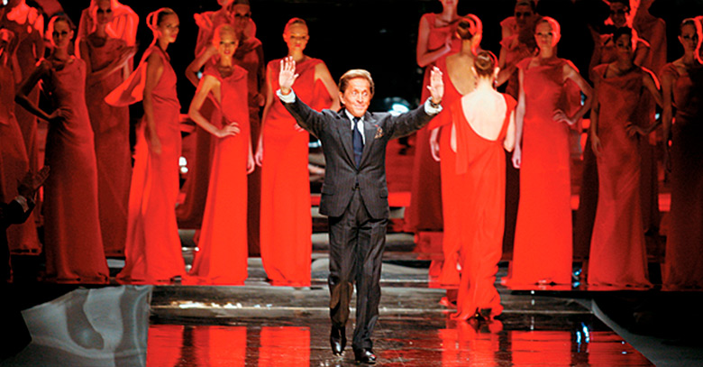 Modelos vestidas de vermelho e estilista Valentino na frente abanando para o público