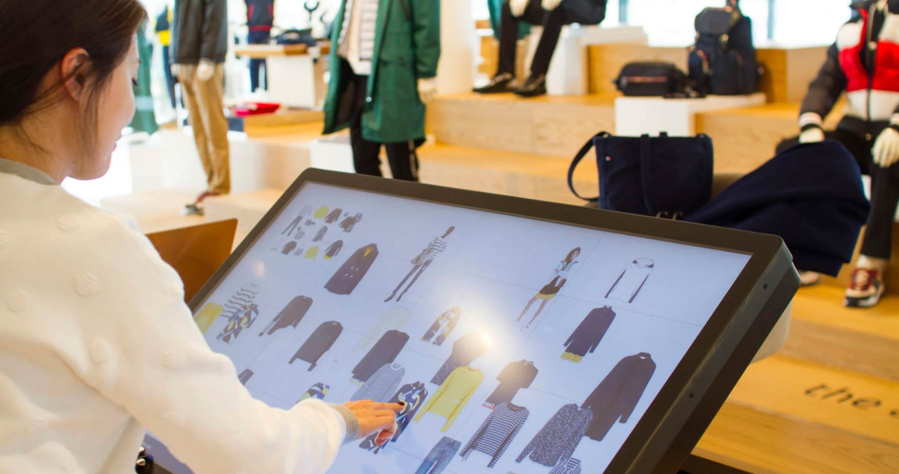 Uma mulher fazendo combinações de peças de roupa através de uma tela grande, representando a inovação digital nas lojas físicas
