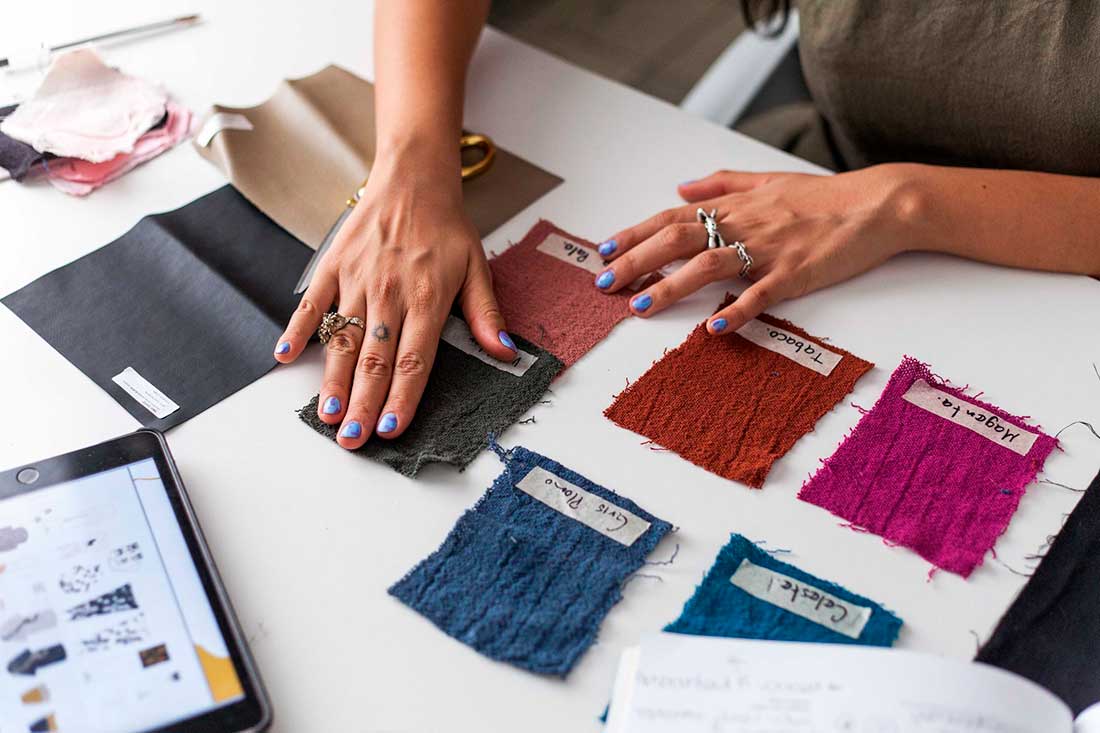 mulher analisando amostras de tecido em cima de uma mesa para escolher a cartela de cores da coleção de moda