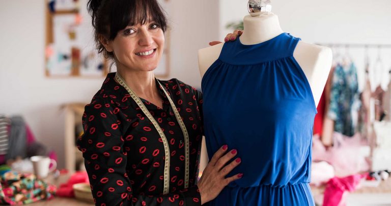 estilista orgulhosa ao lado de vestido produzido para coleção de moda 2022