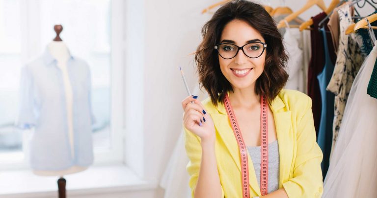 mulher de blazer amarelo em destaque, e ao fundo uma sala de confecção de roupas
