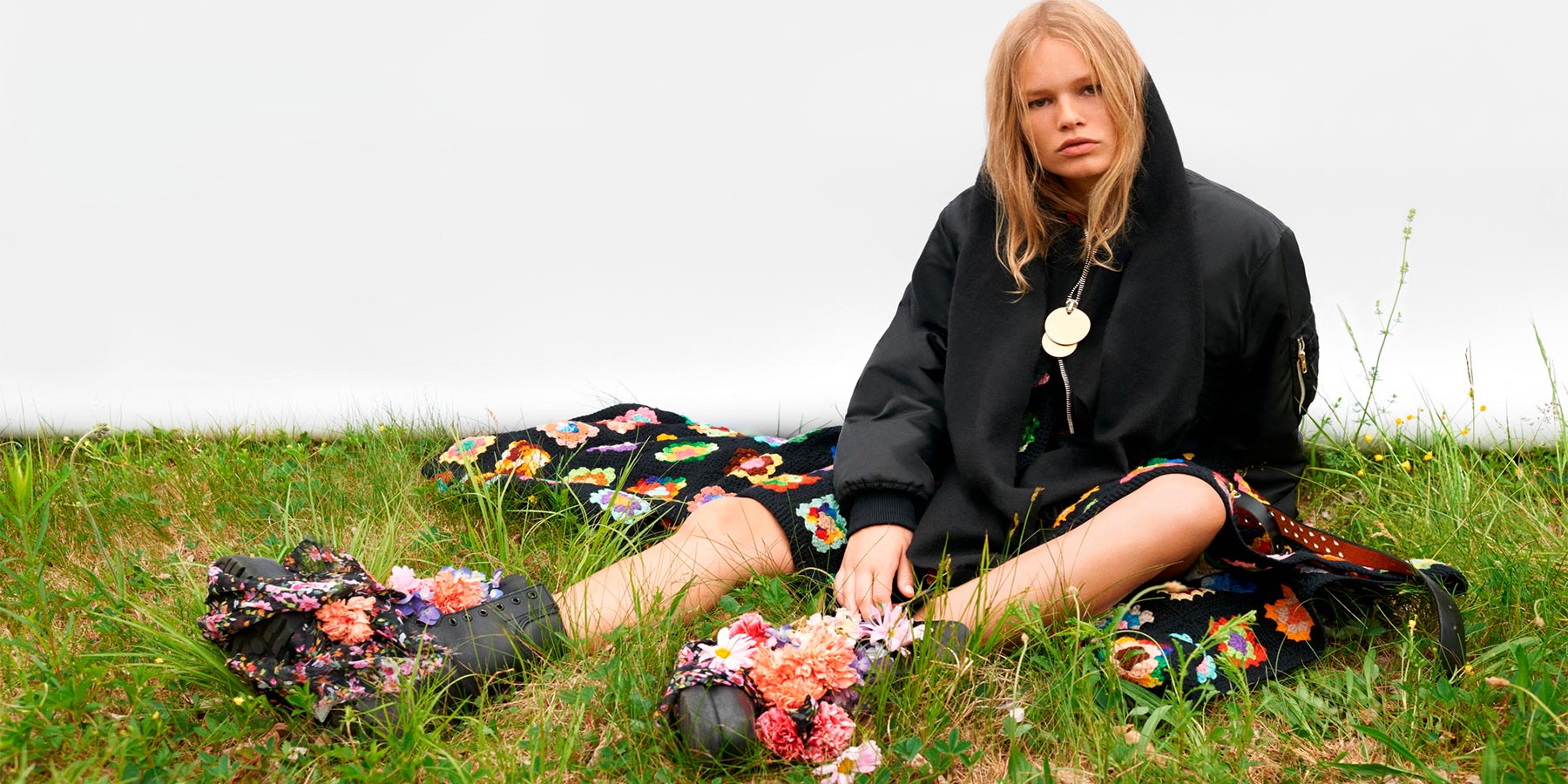 Adolescente com roupas pretas sentada na grama no estilo emo