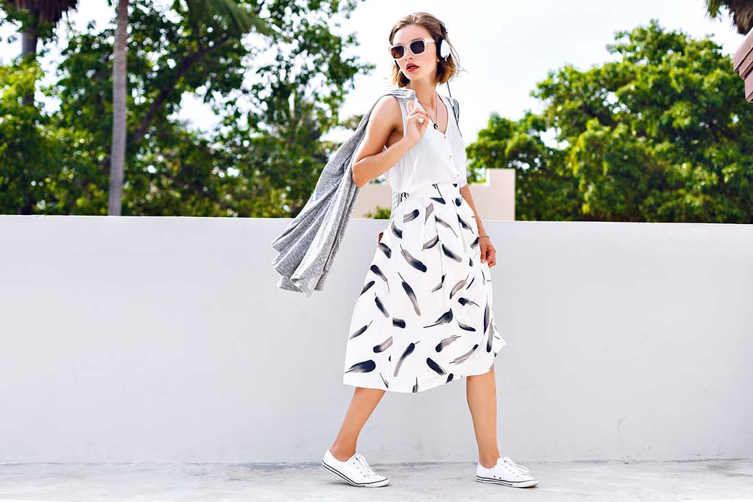 mulher de fone e óculos de sol vestindo saia midi uma das tendências da moda cíclica