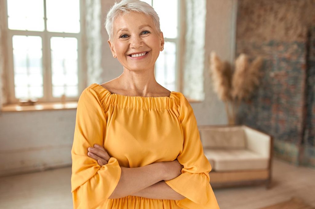 Mulher adulta sorridente e feliz usando roupas no estilo Quiet Luxury, dentro de casa