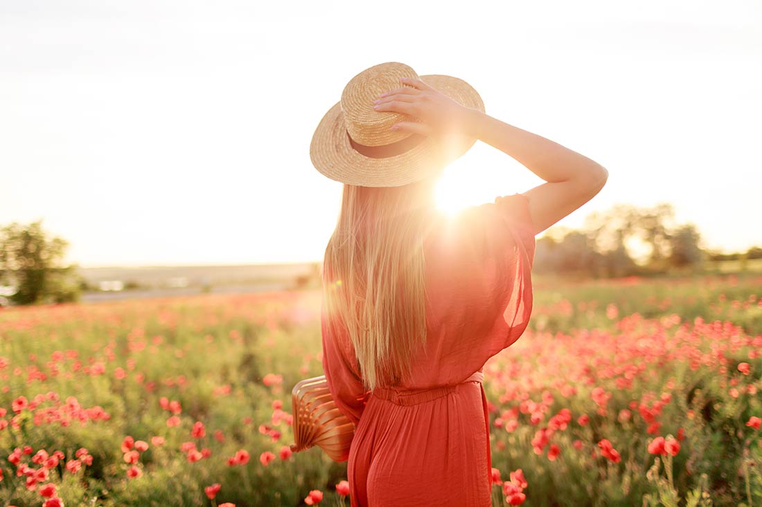 Mulher jovem com vestido vermelho e chapéu no estilo boho chic, passeando no meio das flores