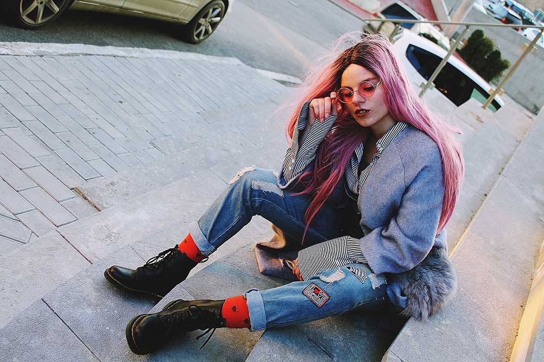 mulher de cabelo colorido, sentada na calçada, usando roupas jeans e posando para foto