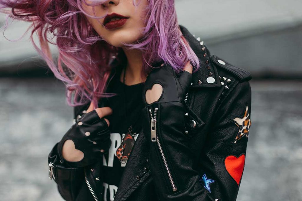 foto close de mulher de cabelo roxo usando jaqueta de couro e luvas com recortes