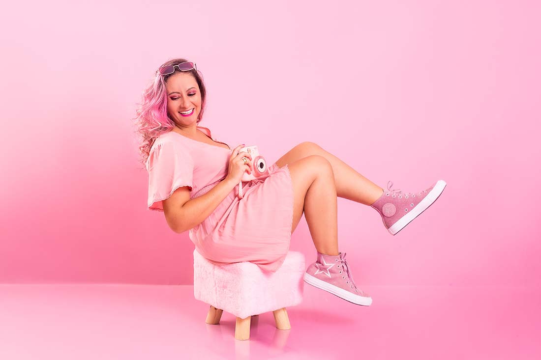 foto de mulher com cabelo rosa, usando um vestido e calçados cor de rosa, em frente a um fundo rosa, representando vários aspectos do barbiecore