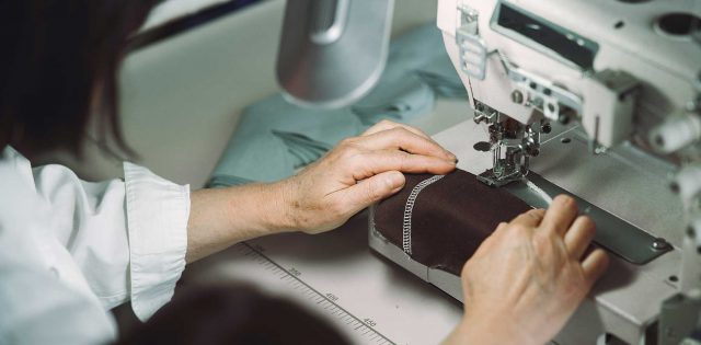 mulher costurando uma etiqueta em uma peça de roupas, seguindo as diretrizes de etiquetagem têxtil