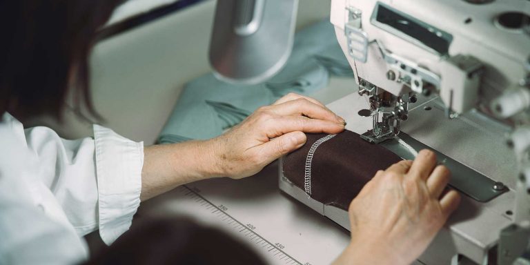 mulher costurando uma etiqueta em uma peça de roupas, seguindo as diretrizes de etiquetagem têxtil